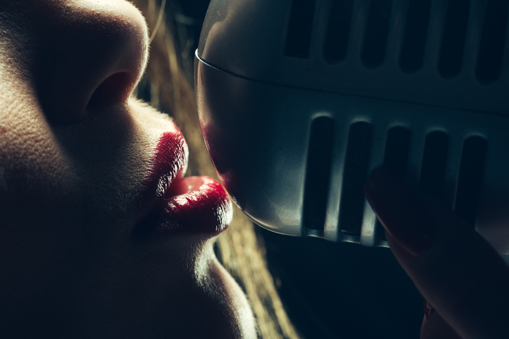 young sexy woman profile with pretty face and red lips singing into studio silver microphone with long hair, closeup